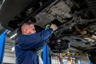 Vidange moteur en garage mécanicien effectue la vidange sous le véhicule avec bac de récupération d’huile