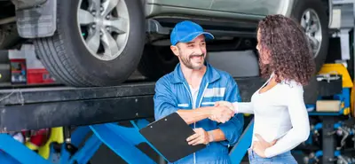 Garagiste et cliente échangeant après une intervention sur une voiture dans un garage automobile