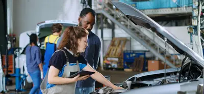 Contrôle du moteur d’un véhicule par une mécanicienne avec un client dans un garage automobile