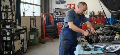 Un garagiste dans un atelier auto réalisant une intervention sous le capot d'une voiture, au niveau de la courroie d’accessoires