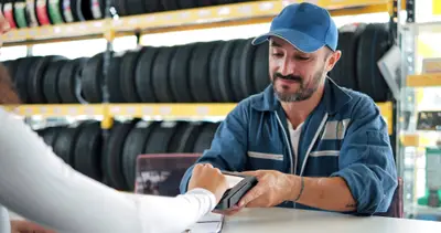 Achat pneus en garage, un mécanicien encaisse un client au comptoir, avec des pneus stockés en arrière-plan