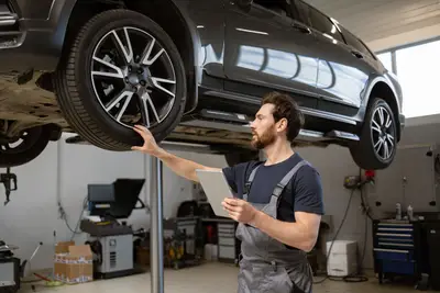 Mécanicien contrôlant un pneu sur un SUV sur pont élévateur, tablette en main, dans un atelier automobile